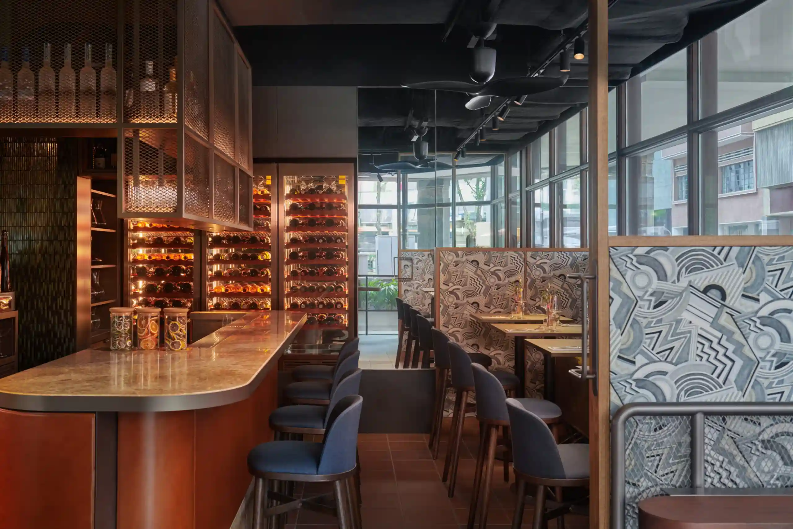 Stylish wine bar with illuminated bottle display, counter seating and patterned partitions.