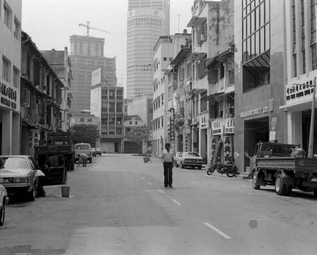 A man standing in the middle of Carpenter Street in Singapore shot in black and white
